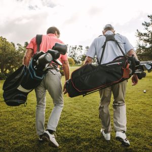 Rear view of two senior golf players walking together in the golf course with their golf bags. Senior golfers walking out of the course after the game.