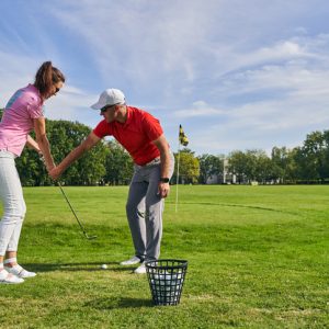 Experienced male instructor teaching a young woman to hold a club correctly during the game